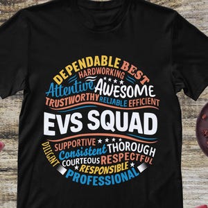 May include: Black t-shirt with a colorful design. The design includes the text "EVS SQUAD" in white, surrounded by words like "Dependable," "Awesome," and "Professional." The shirt is a crew neck style.