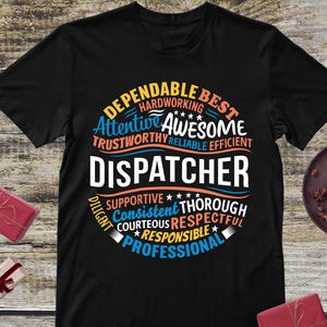 May include: Black t-shirt with a circular design featuring the word "DISPATCHER" in large white letters. Surrounding the word are adjectives like "Dependable," "Awesome," and "Professional" in blue and orange.