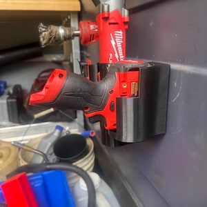 May include: A red and black Milwaukee FUEL power tool is mounted on a black holder. The tool is attached to a wall. Other tools and supplies are visible in the background, including a wire brush and a red traffic cone.