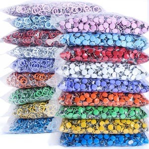 Puede incluir: Una pila de bolsas de plástico transparente llenas de chinchetas de cabeza redonda y coloridas. Las chinchetas vienen en una variedad de colores, incluyendo rosa, azul, rojo, plateado, morado, naranja, verde, amarillo y azul.