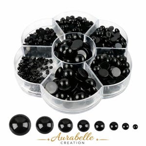 May include: A clear, flower-shaped container filled with various sizes of black, glossy, flat-backed cabochons. Below the container are several individual cabochons, ranging in size. The text "Aurabelle Creation" is printed in gold.