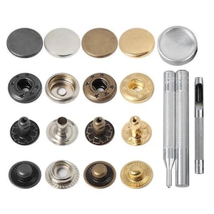 May include: A set of metal snap fasteners in black, silver, bronze, and gold finishes, arranged in rows with matching components. The collection includes circular caps, sockets, studs, and posts, accompanied by three metal setting tools for installation.