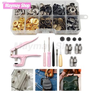 May include: A clear plastic storage box containing assorted metal snap buttons in gold, silver, black, and bronze finishes. Includes a pink hand-held fastener tool, metal punches, screwdrivers, and various metal dies for attaching fasteners to fabric.
