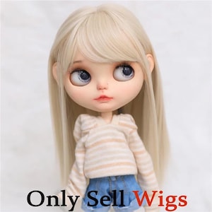 May include: A doll with long, straight, pale blonde hair and bangs, featuring large, round, light blue eyes and a small nose. The doll wears a long-sleeved, beige and white horizontal striped hooded sweatshirt and blue denim shorts.