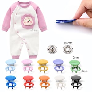 May include: A baby's white and pink onesie with a lion applique and the text "LLG. BABY". The image also shows various colored snap fasteners, including blue, pink, yellow, purple, green, red, orange, white, and black. The snap fasteners are 9.5mm and 10mm in diameter.