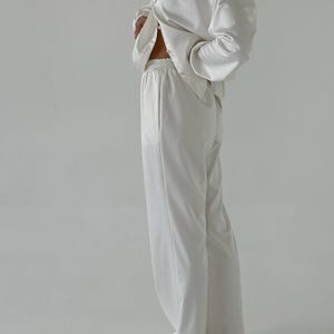 May include: A white satin pyjama set with a long-sleeved button-up shirt and wide-leg trousers.