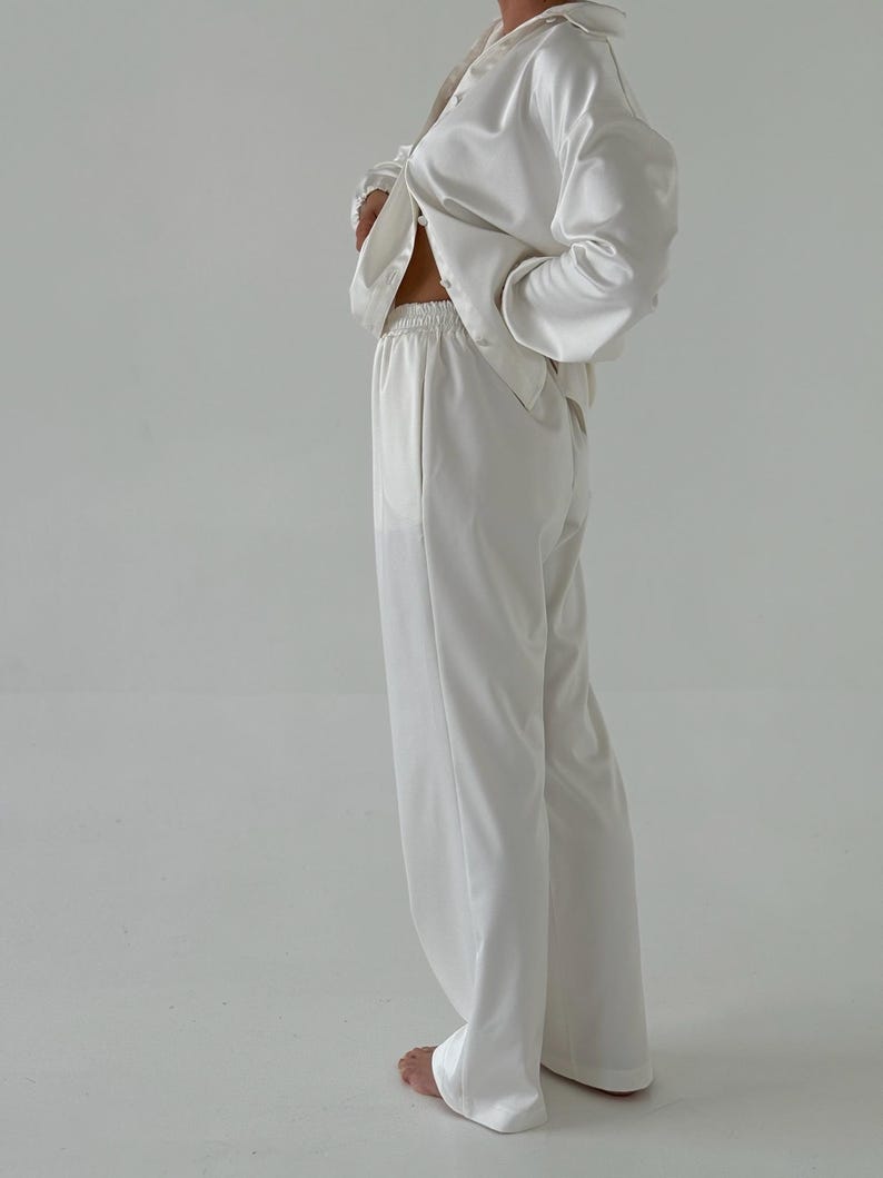 May include: A white satin pyjama set with a long-sleeved button-up shirt and wide-leg trousers.