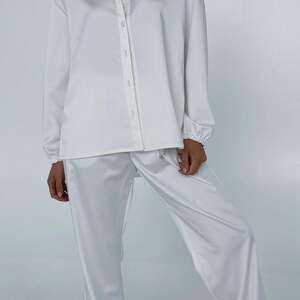 May include: A white satin pyjama set with a long-sleeved button-up shirt and matching trousers.