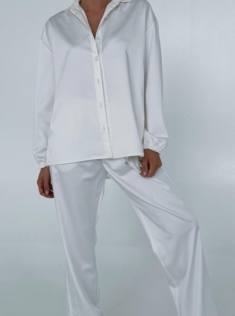 May include: A white satin pyjama set with a long-sleeved button-up shirt and matching trousers.