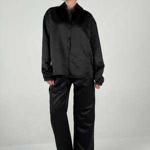 May include: A black satin shirt and matching trousers. The shirt has a collared neckline and long sleeves. The trousers have a straight leg.