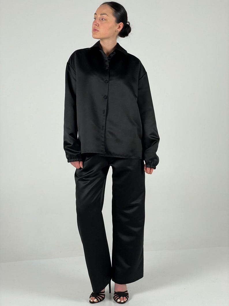 May include: A black satin shirt and matching trousers. The shirt has a collared neckline and long sleeves. The trousers have a straight leg.