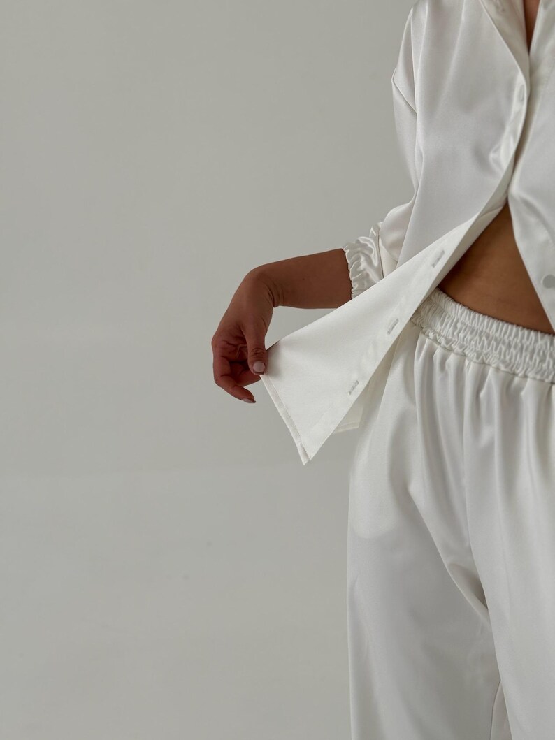 May include: A white satin pyjama set with a long-sleeved button-up shirt and matching trousers.