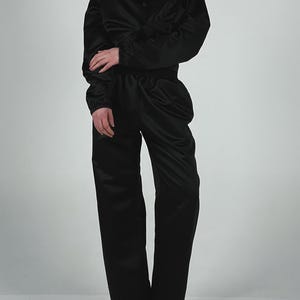 May include: A black satin jumpsuit with a button-up shirt style top and long trousers. The jumpsuit has a relaxed fit and is made of a soft, silky fabric.