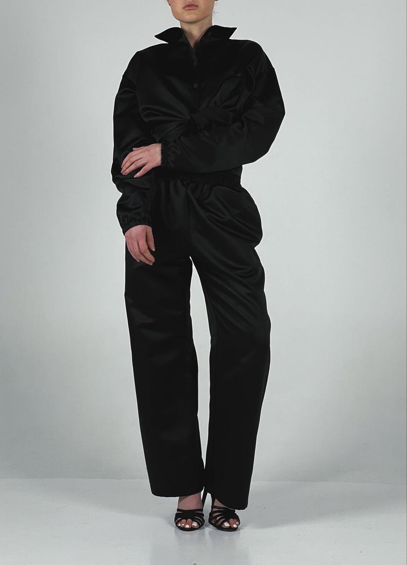 May include: A black satin jumpsuit with a button-up shirt style top and long trousers. The jumpsuit has a relaxed fit and is made of a soft, silky fabric.