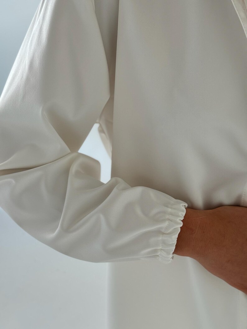 May include: A white long-sleeved shirt with a gathered elastic cuff at the wrist.