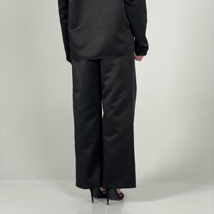 May include: Black wide-leg trousers with a satin finish. The trousers are tailored and have a straight leg.