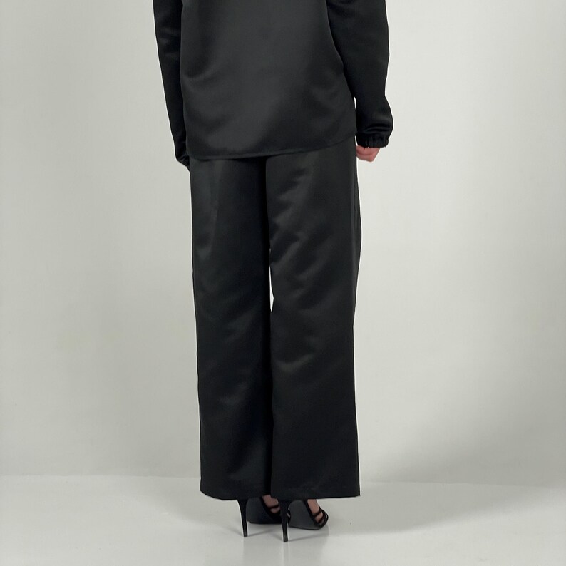 May include: Black wide-leg trousers with a satin finish. The trousers are tailored and have a straight leg.
