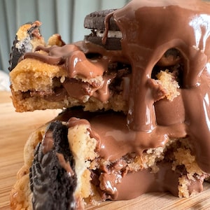 Peut inclure: Gros plan sur un cookie géant avec un nappage au chocolat. Le cookie est fourré au chocolat et contient un Oreo. Le cookie est coupé en deux, révélant l'intérieur.