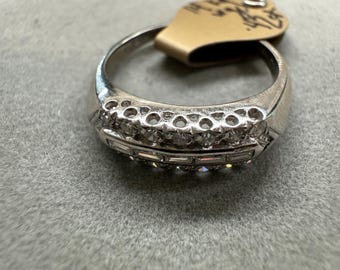 Könnte beinhalten: Ein silberner Ring mit zwei Reihen kleiner, klarer Edelsteine und einer Reihe rechteckiger Steine. Der Ring liegt auf einer grauen Oberfläche, mit einem Preisschild.
