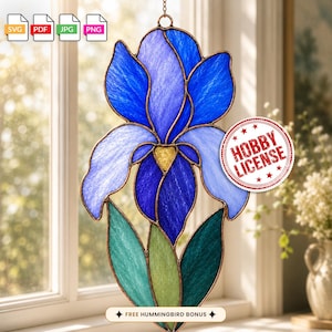 Op de afbeelding: Een glas-in-lood zonnevanger in de vorm van een irisbloem met blauwe, paarse en groene glassegmenten gehouden door koperkleurige metalen lijnen. Een rode stempel toont HOBBY LICENSE en een label toont FREE HUMMINGBIRD BONUS.