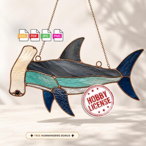May include: A stained glass hammerhead shark suncatcher with copper foil edges, featuring textured cream, teal, dark blue, and black glass panels. The design includes icons for SVG, PDF, JPG, PNG files, a Hobby License stamp, and text reading FREE HUMMINGBIRD BONUS.
