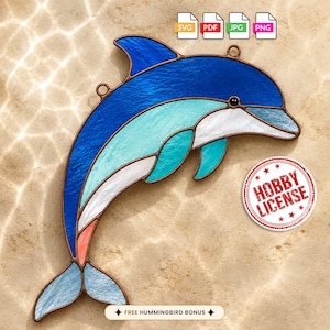 May include: A stained glass dolphin suncatcher featuring deep blue, turquoise, and white glass segments joined by copper foil. The design includes two small metal loops for hanging. A circular stamp reads HOBBY LICENSE, and text states FREE HUMMINGBIRD BONUS.