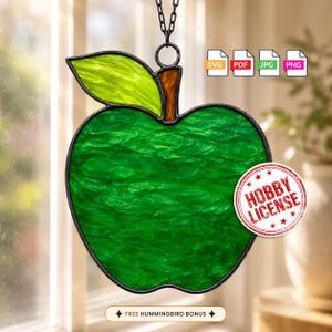 Könnte beinhalten: Ein Apfel-Sonnenfänger aus Buntglas mit einem texturierten dunkelgrünen Körper, einem hellen lindgrünen Blatt und einem braunen Stiel. Das Stück hat einen schwarzen Metallrahmen und eine Aufhängungskette. Enthält SVG-, PDF-, JPG-, PNG-Dateisymbole und ein Hobby-Lizenz-Siegel.