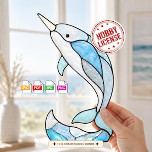 May include: A stained glass narwhal suncatcher featuring shades of light and dark blue with a white tusk. The design includes icons for SVG, PDF, JPG, and PNG file formats, a red circular stamp reading HOBBY LICENSE, and text reading FREE HUMMINGBIRD BONUS.