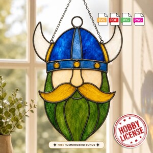 May include: A stained glass suncatcher shaped like a Viking head with a blue helmet, white horns, a cream-colored face, a yellow mustache, and a green beard. The piece hangs from a metal chain and includes digital file icons and a hobby license seal.