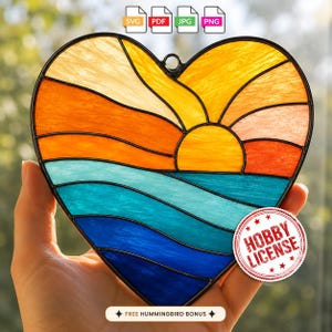 May include: A heart-shaped stained glass suncatcher featuring a sunset over the ocean. The design includes yellow, orange, and red glass segments representing the sun and sky, with blue and teal glass segments depicting the sea, all joined by black metal lines.