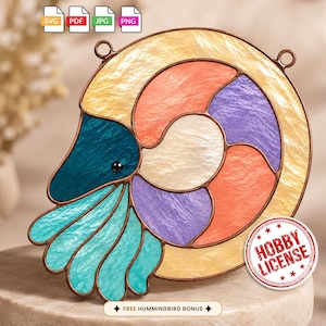 May include: A stained glass nautilus shell suncatcher featuring textured panels in shades of cream, peach, purple, teal, and light blue, outlined in dark metal solder. Two small metal rings are attached to the top for hanging purposes.