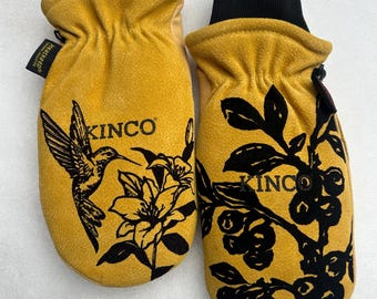 May include: A pair of yellow Kinco mittens with black cuffs. One mitten features a black hummingbird and flower design, the other has a black berry branch design. The brand name "KINCO" is printed on both mittens.