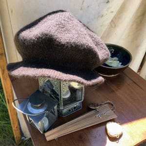 May include: A brown knitted hat sits on a wooden table with a small lantern, a wooden fan, and a silver charm.