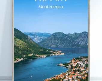 May include: A framed poster with a scenic view of Kotor, Montenegro. The poster features a blue bay with a town built along the shoreline, surrounded by green mountains. The text "Kotor, Montenegro" is printed in white at the top of the poster.