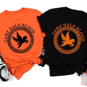 May include: Two t-shirts featuring the text "Camp Half-Blood" and a winged horse design. The shirts are orange and black.
