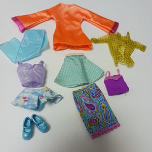 Peut inclure: Ensemble de vêtements de poupée comprenant un haut orange à bordure rose, une écharpe bleu clair, un haut lavande à paillettes, une jupe verte, une chemise jaune à carreaux, une jupe bleue à motifs cachemire, un haut violet, une jupe à fleurs et des chaussures bleues.