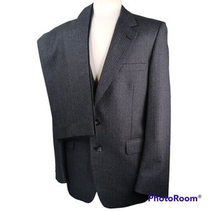May include: A charcoal gray pinstripe suit displayed on a mannequin. The suit includes a two-button blazer with a notched lapel and a pair of matching trousers. The fabric has a subtle vertical stripe pattern.