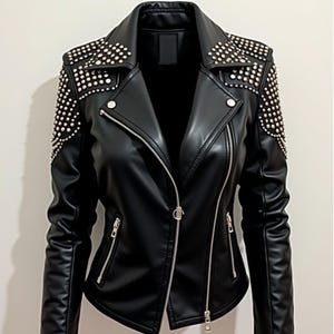 May include: Black faux leather jacket with silver zippers and studded shoulder accents. The jacket features a notched collar, an asymmetrical zip closure, and multiple zippered pockets. A stylish outerwear piece.