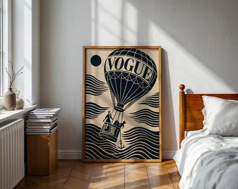 May include: A framed art print featuring a black and beige design. The artwork depicts a hot air balloon with the word "VOGUE" on it, floating above stylized waves. A black circle and a small basket with figures are also visible.