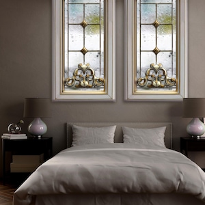 Puede incluir: Dos ventanas con marco dorado con paneles de vidrieras que presentan un patrón de diamante y adornos dorados ornamentados. Las ventanas están colocadas contra una pared marrón claro sobre una cama con ropa de cama blanca.