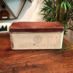 May include: A vintage white metal bread box with a red lid. The box has a small, round, perforated vent on the front.