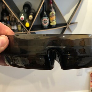 May include: A dark brown glass bowl with a unique, wave-like design. The bowl has a wide, shallow shape and a smooth, glossy finish.
