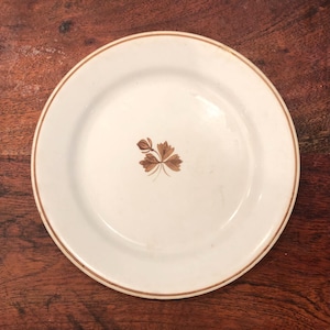 以下が含まれることがあります： 茶色の葉のデザインが施された白いセラミック製のプレート。プレートは金色の縁取りがされています。