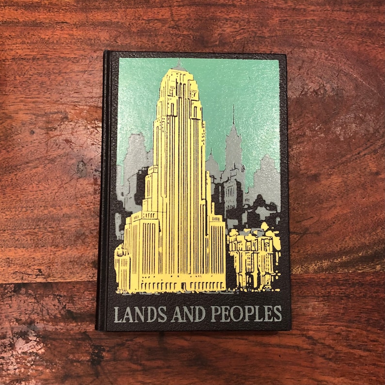 May include: A black hardback book with a yellow and green illustration of a city skyline. The book title is "Lands and Peoples".