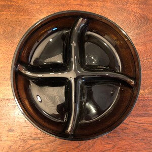 May include: A dark brown glass serving dish with four divided sections. The dish is round and has a smooth, glossy finish.