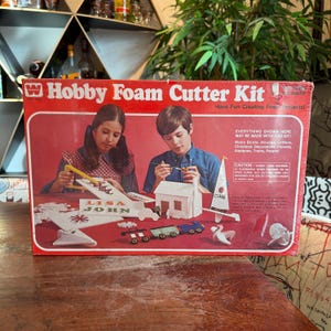 May include: A vintage Hobby Foam Cutter Kit in a red box, with illustrations of children crafting foam projects. The kit includes instructions and materials to create boats, houses, letters, and more. The box reads "Hobby Foam Cutter Kit" and "Have Fun Creating Foam Projects!"