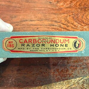 May include: A vintage Carborundum Razor Hone, with a red and gold label. The label includes the text "CARBORUNDUM BRAND RAZOR HONE" and "MFD. BY THE CARBORUNDUM CO. NIAGARA FALLS, N.Y., U.S.A."
