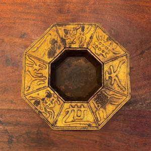May include: Octagonal gold-colored metal ashtray with intricate designs and Chinese characters around the rim.
