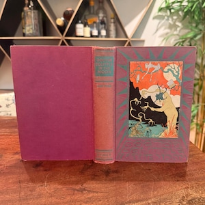May include: A hardcover book titled Doctor Dolittle in the Moon by Hugh Lofting, published by Stokes. The cover is a deep magenta with a teal border and a central illustration featuring a figure with antlers, a top hat, and a moonlit landscape.