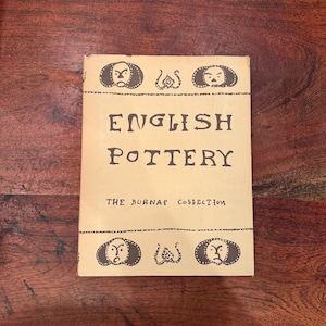 Peut inclure: Un livre vintage intitulé "ENGLISH POTTERY" de la collection Burnap. La couverture est de couleur beige clair avec du texte et des éléments décoratifs marron foncé. Le livre est rectangulaire et semble en bon état.